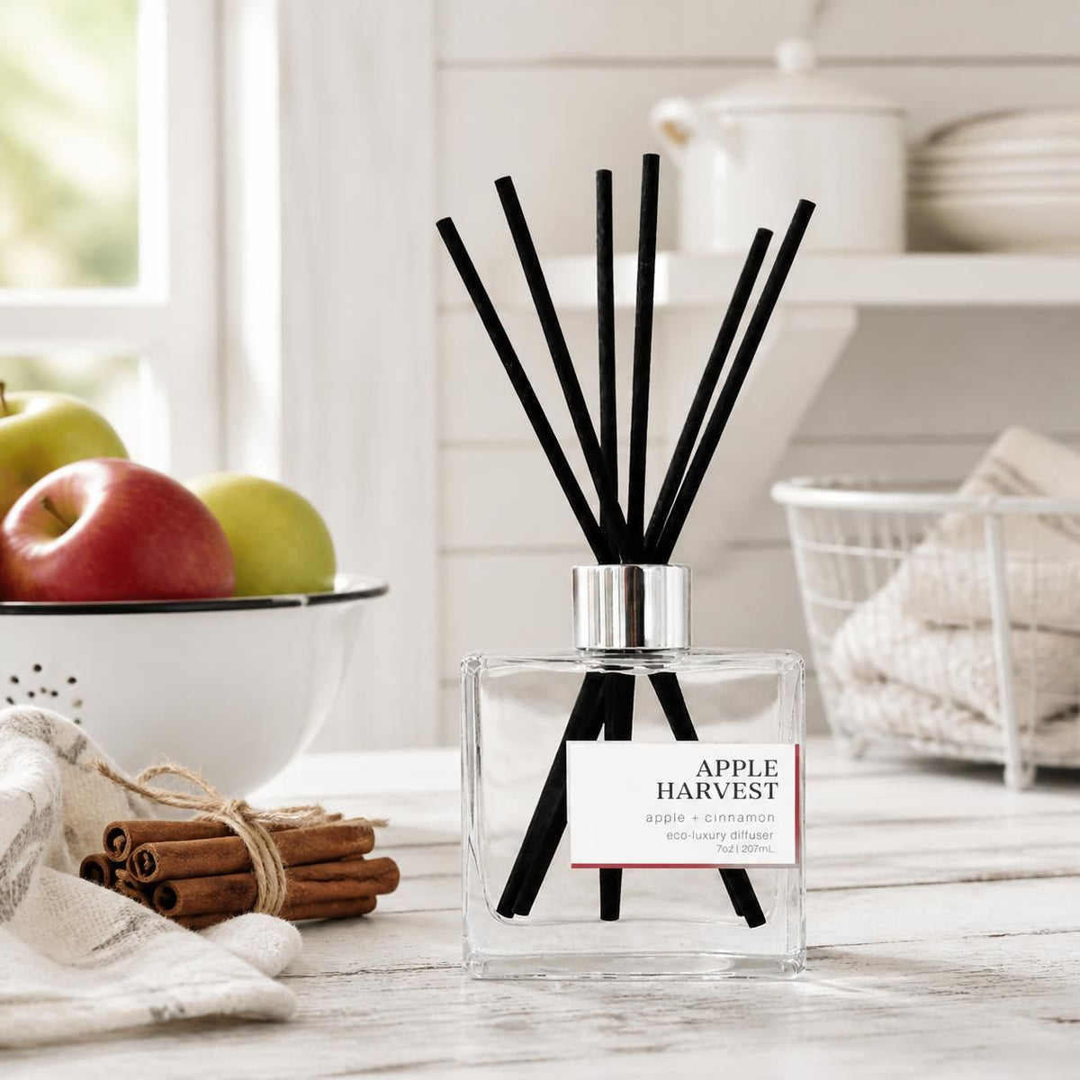Green Koala Apple Harvest non-toxic reed diffuser on a white rustic farmhouse kitchen counter with fresh apples and cinnamon sticks