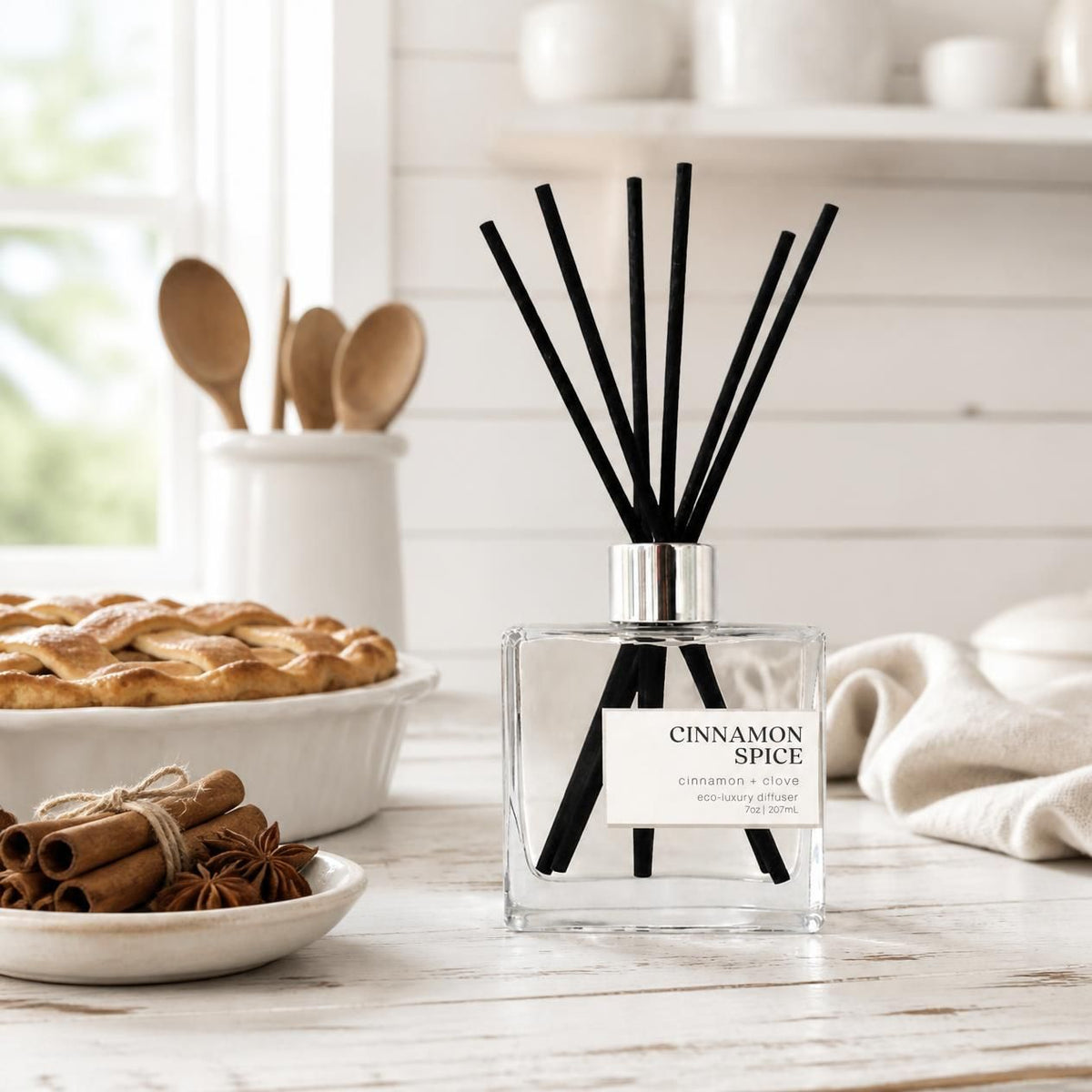 Green Koala Cinnamon Spice non-toxic reed diffuser on a white farmhouse kitchen counter with cinnamon sticks and a fresh pie