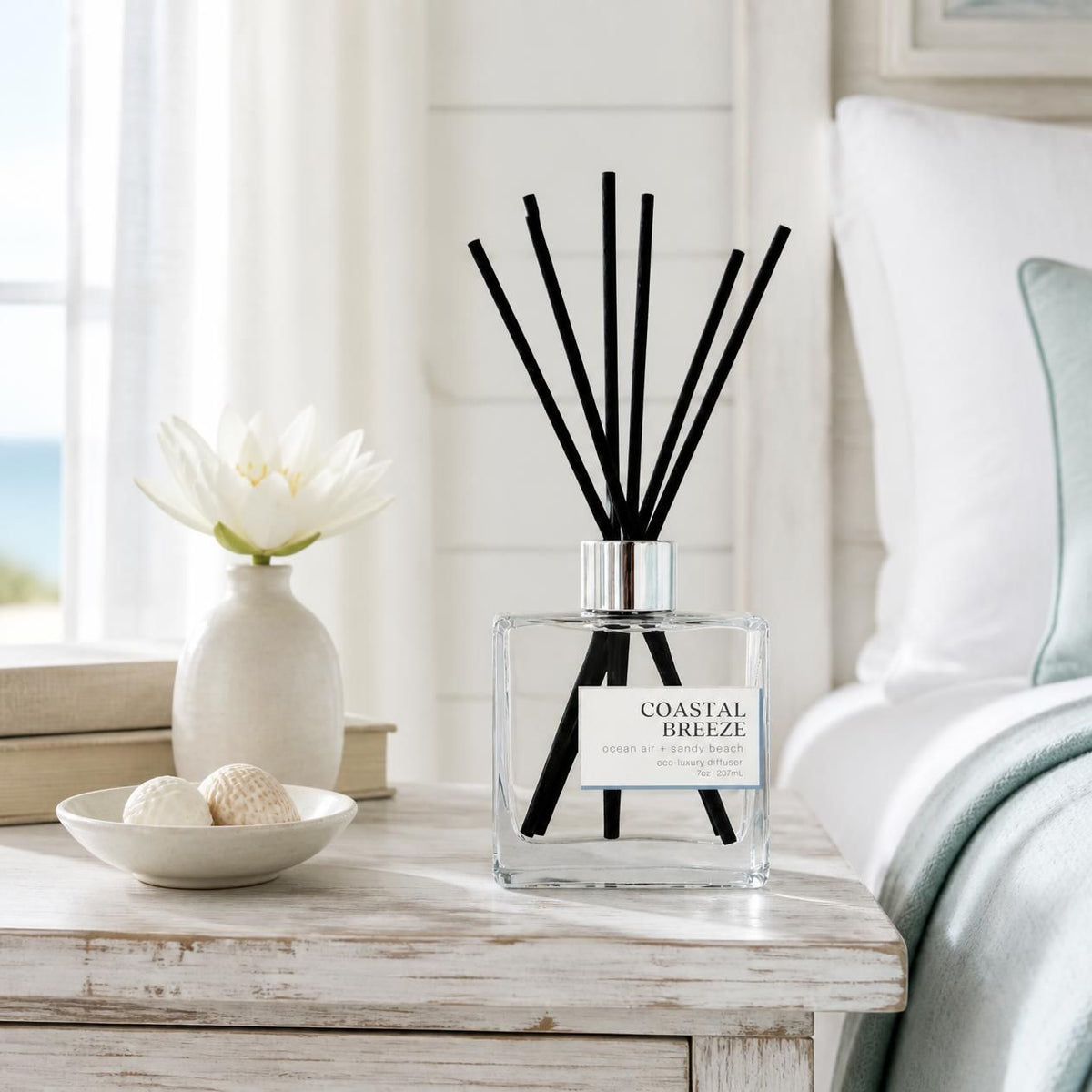 Green Koala Coastal Breeze non-toxic reed diffuser on a white coastal farmhouse nightstand with seashells and white lilies