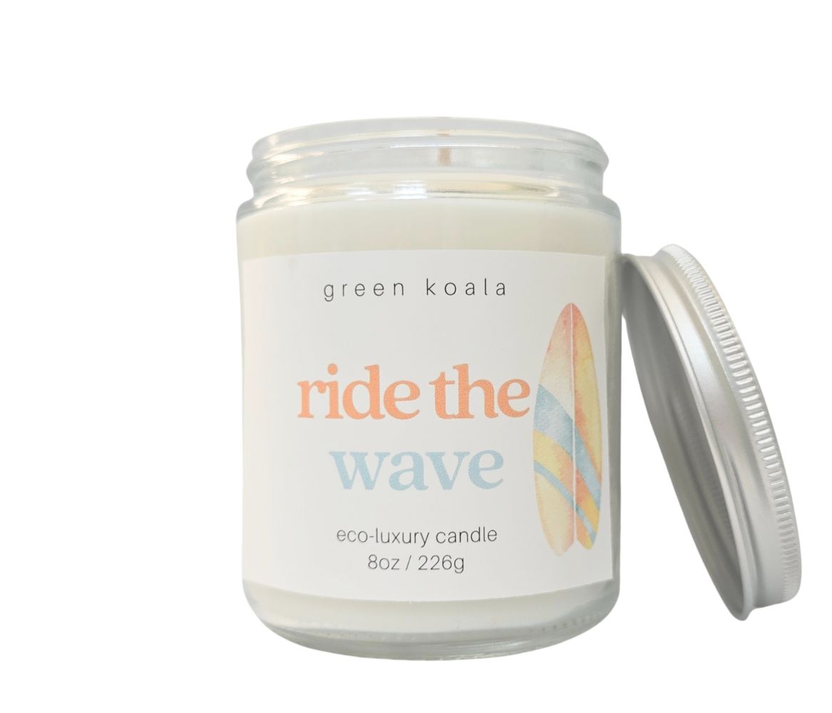 Ride the Wave candle with lid leaning on the side of the jar, highlighting beachy branding and coastal candle design. Made with coconut wax.