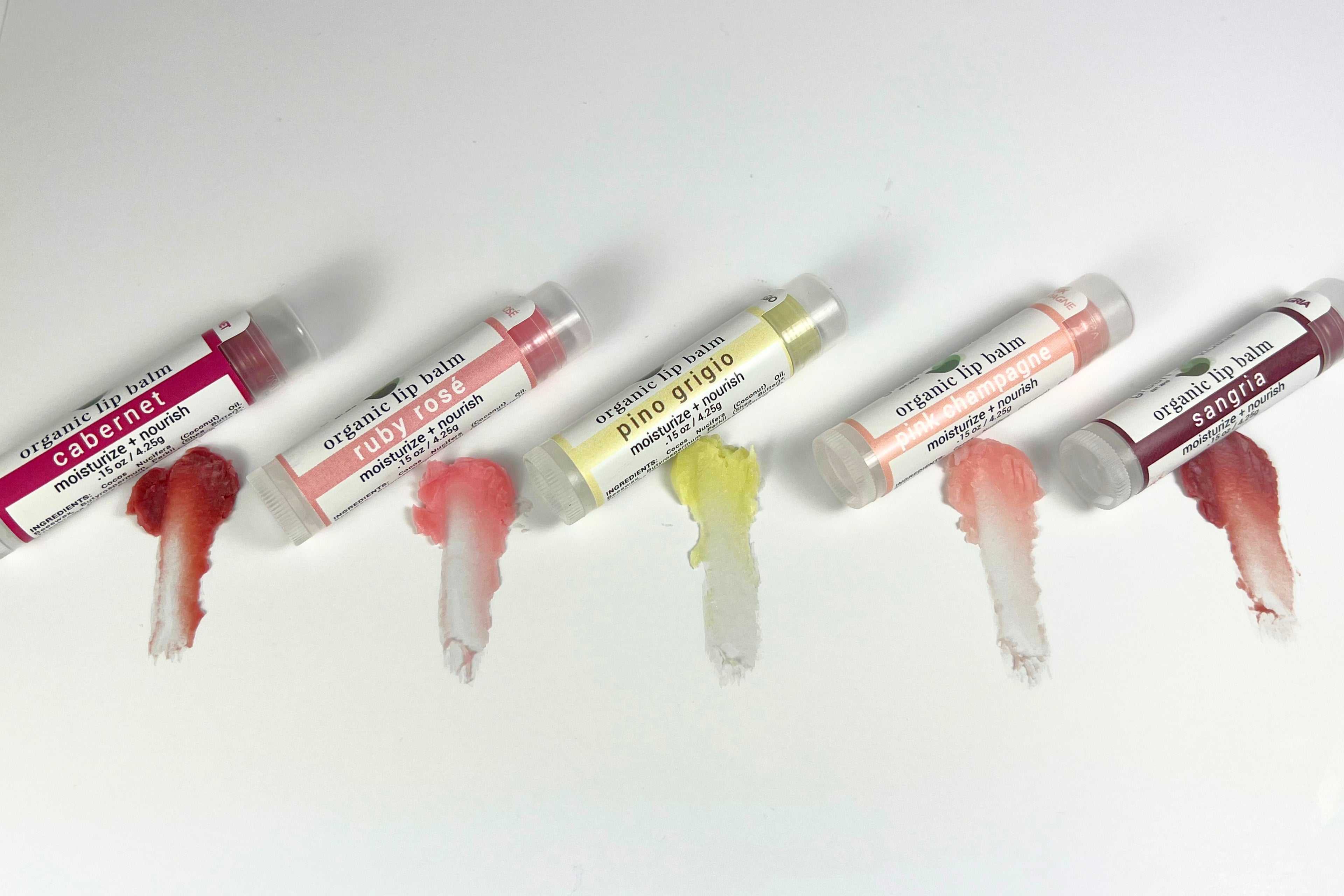 A display of tinted, wine-flavored lip balms next to neutral colored swatches of the corresponding shea butter lip balms. 