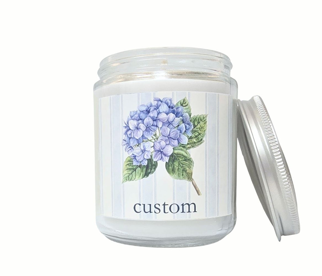 Personalized 8oz coastal candle with hydrangea stem and blue striped label, custom town name, hand-poured in eco-friendly coconut wax blend.