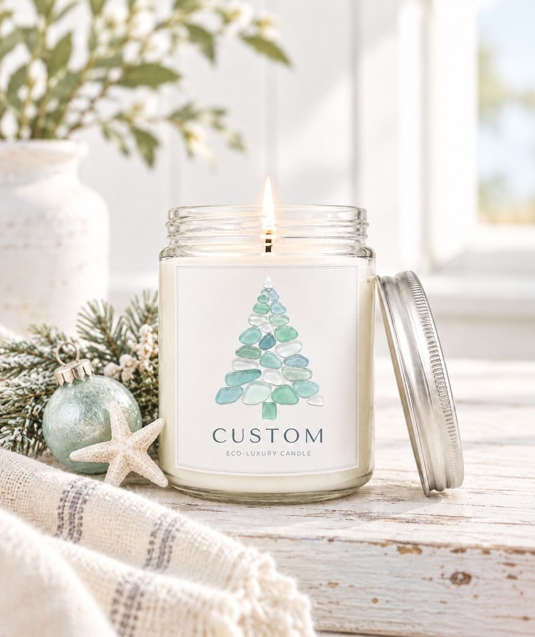 Green Koala personalized sea glass Christmas tree 8oz candle with custom coastal town name label, lit, with silver lid in a rustic farmhouse setting. 
