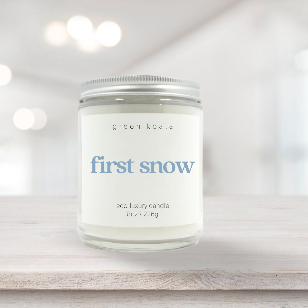 Image of First Snow candle in a glass jar with silver lid on a wooden shelf. 