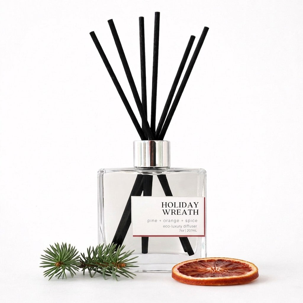 A clear glass reed diffuser bottle with black reeds and a silver cap, labeled &