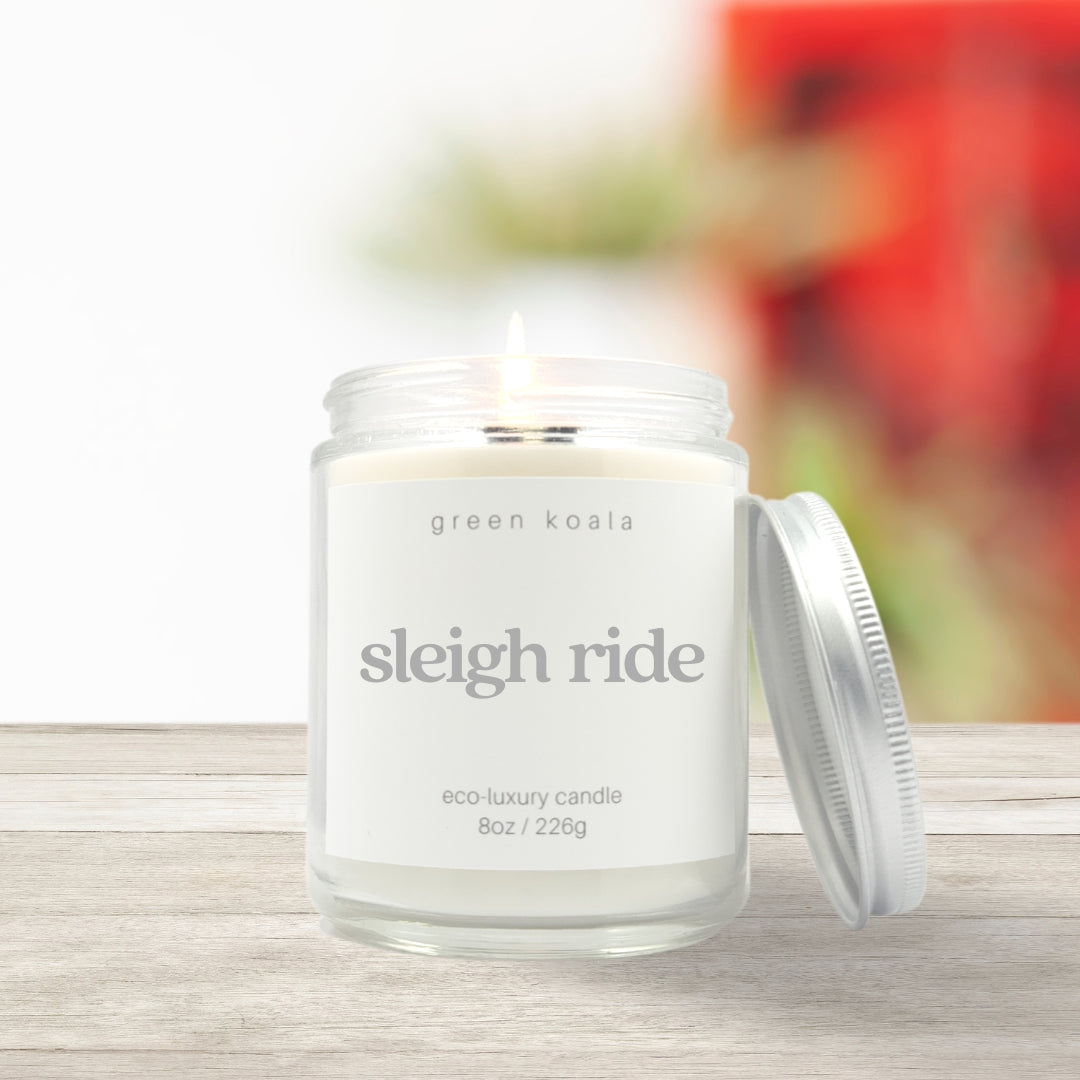 Image of Sleighride candle in a glass jar with silver lid resting on the side on a wooden shelf.  