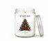 Personalized 8oz Christmas candle in a clear glass jar with an evergreen tree label, pinecones, red berries and bow, silver lid leaning beside it