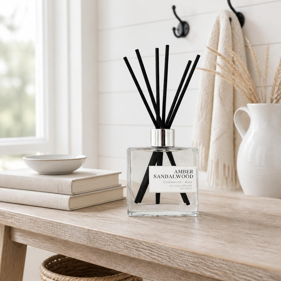 Green Koala Amber Sandalwood non-toxic reed diffuser with black fiber reeds on a side table in an entry way. 