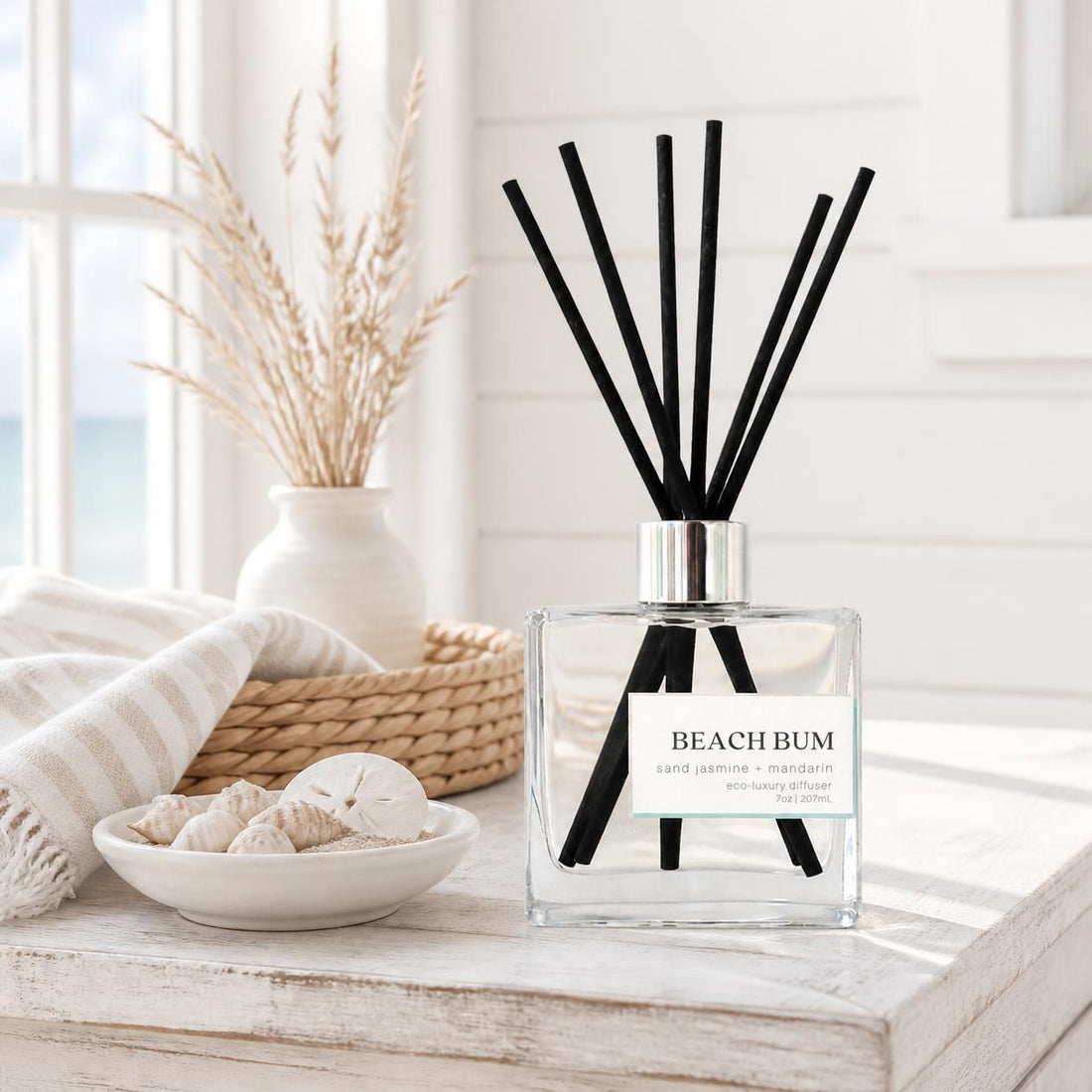 Green Koala Beach Bum non-toxic reed diffuser on a white rustic table in a sunny coastal farmhouse sunroom with seashells