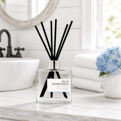 Green Koala Blue Hydrangea non-toxic reed diffuser on a white farmhouse bathroom vanity with white towels and a blue hydrangea