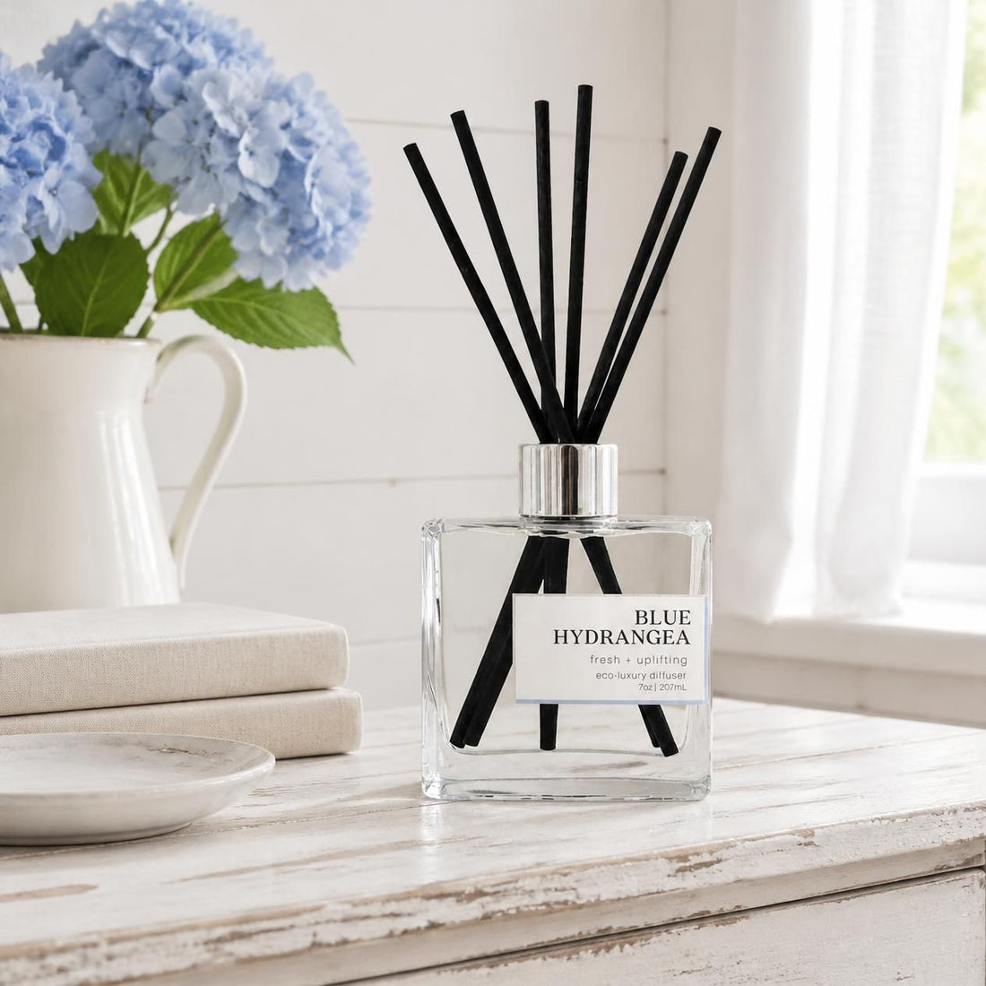Green Koala Blue Hydrangea non-toxic reed diffuser on a white rustic farmhouse dresser with fresh blue hydrangeas