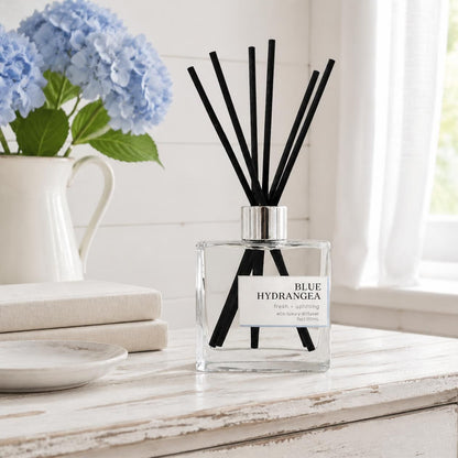 Green Koala Blue Hydrangea non-toxic reed diffuser on a white rustic farmhouse dresser with fresh blue hydrangeas