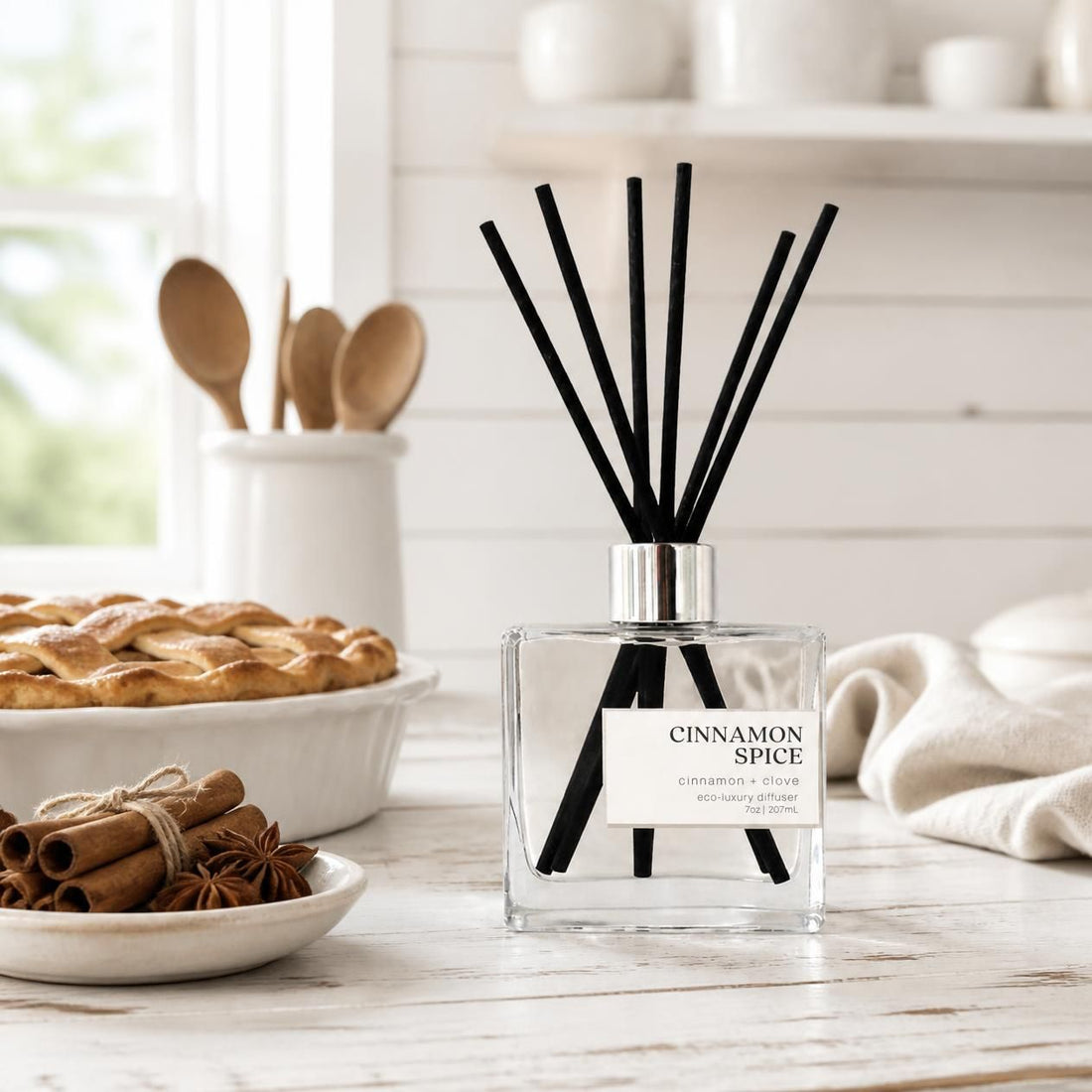 Green Koala Cinnamon Spice non-toxic reed diffuser on a white farmhouse kitchen counter with cinnamon sticks and a fresh pie