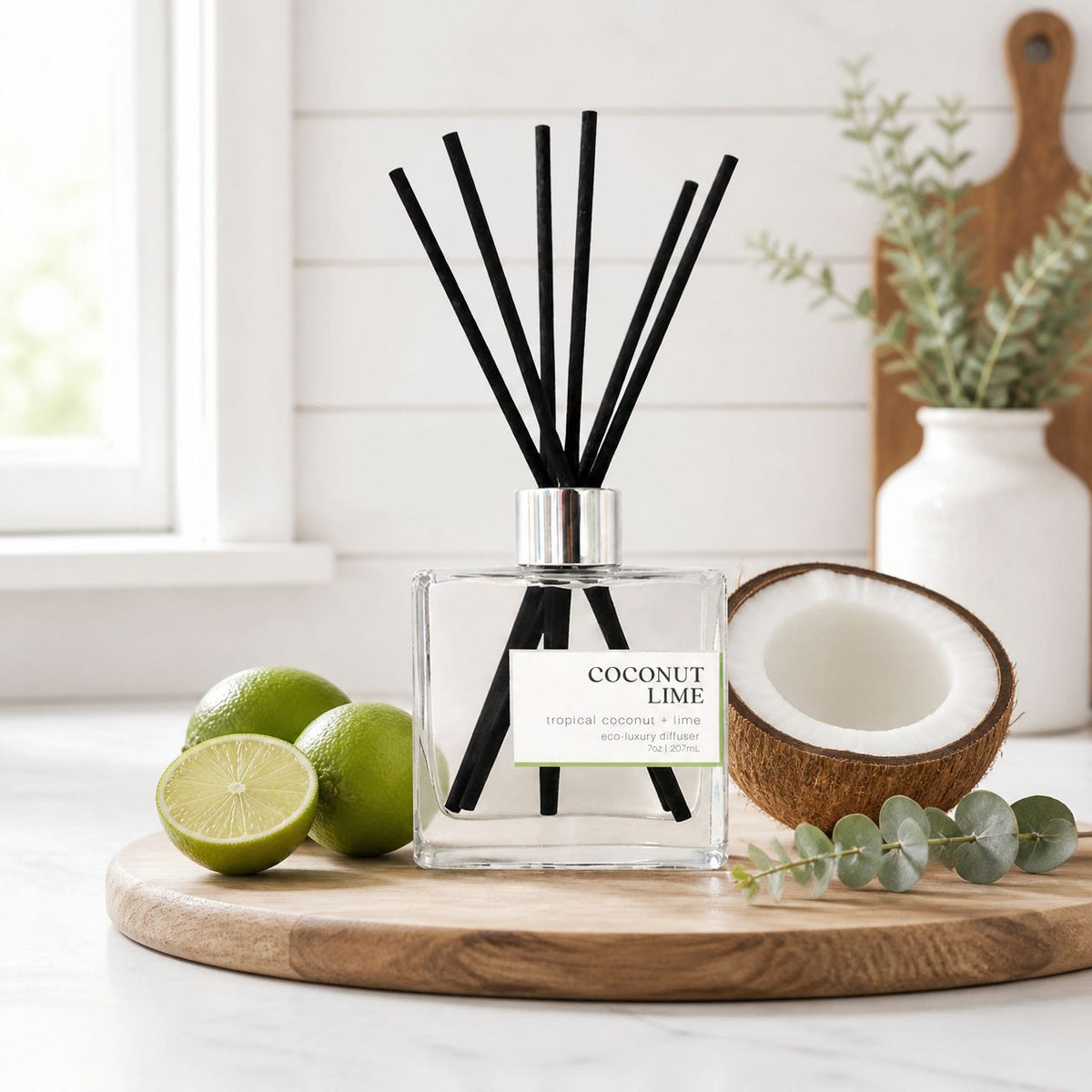 Coconut Lime non-toxic reed diffuser on a wood board with fresh limes and a halved coconut in a bright farmhouse kitchen