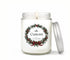 Personalized 8oz holiday candle in a clear glass jar with an evergreen wreath label, red berries and bow, silver lid leaning beside it