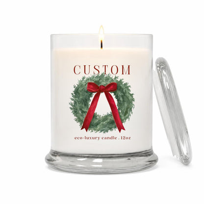 Green Koala personalized holiday wreath 12oz candle with cranberry bow and custom town name label, lit, with glass lid on a white background