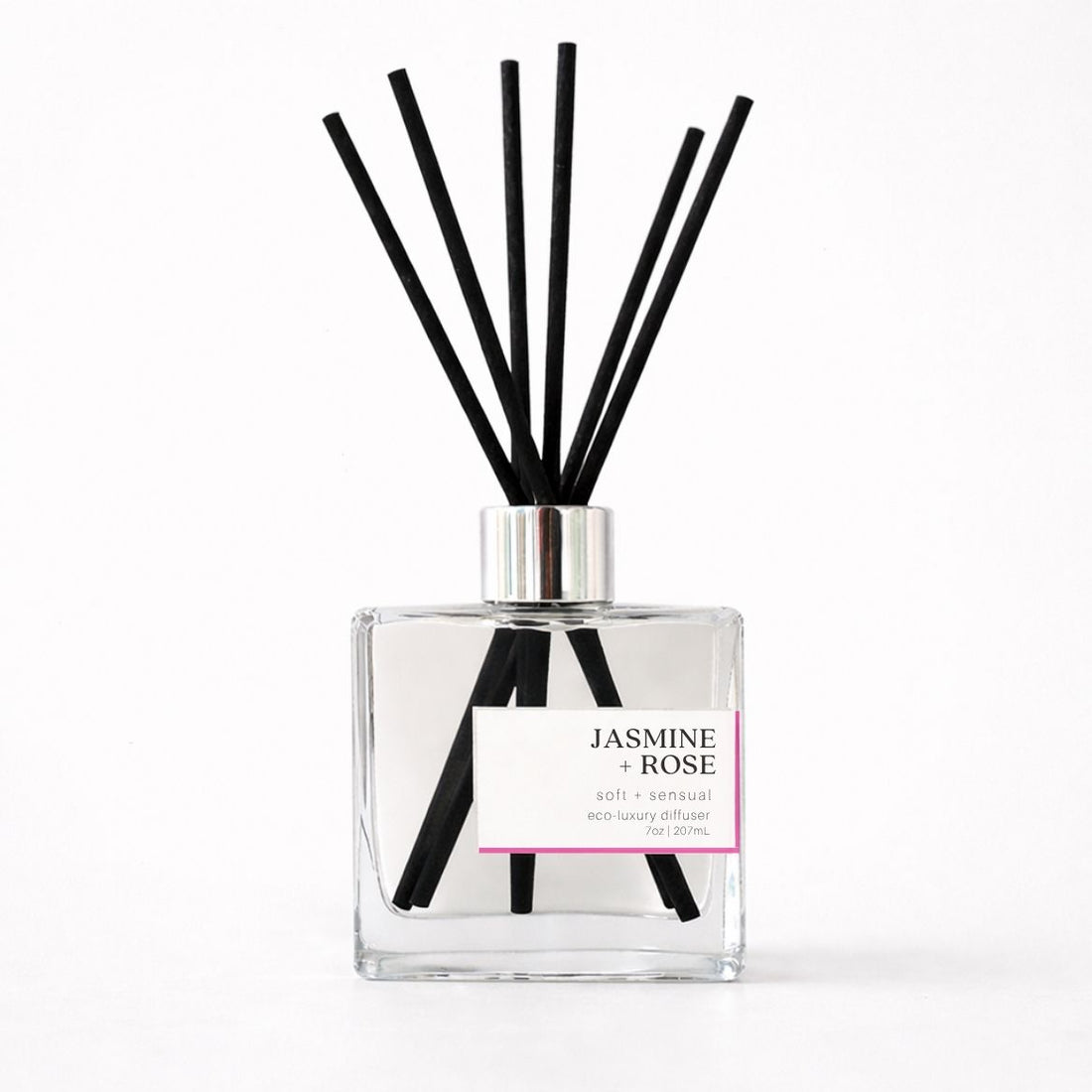 Clear diffuser bottle with black reeds on a white background with Jasmine + Rose Label. 