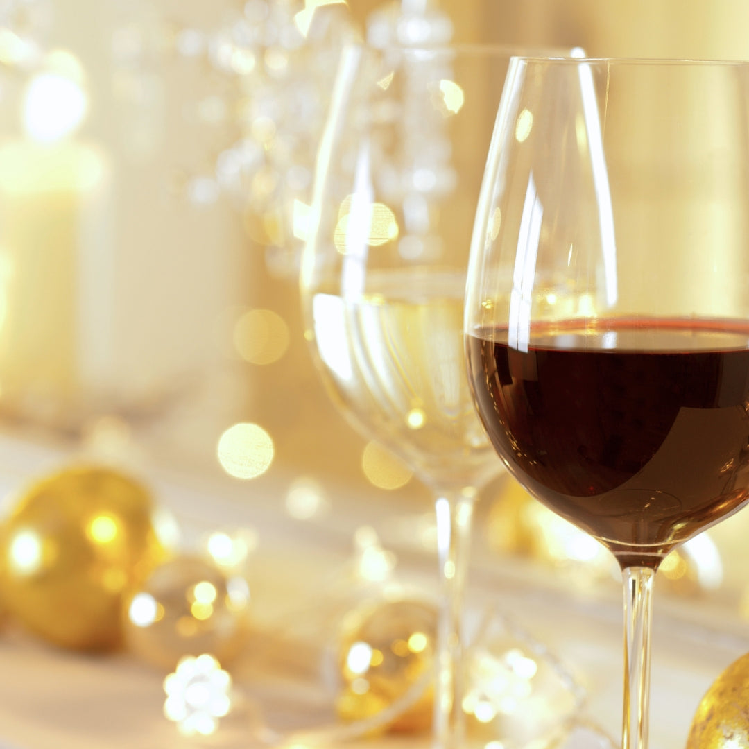 Photo of a glass of red wine in front of a glass of white wine with a gold background. 