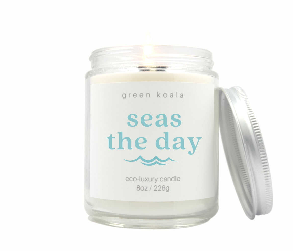 Image of Seas the Day candle in a glass jar with silver lid burning with a white background. 