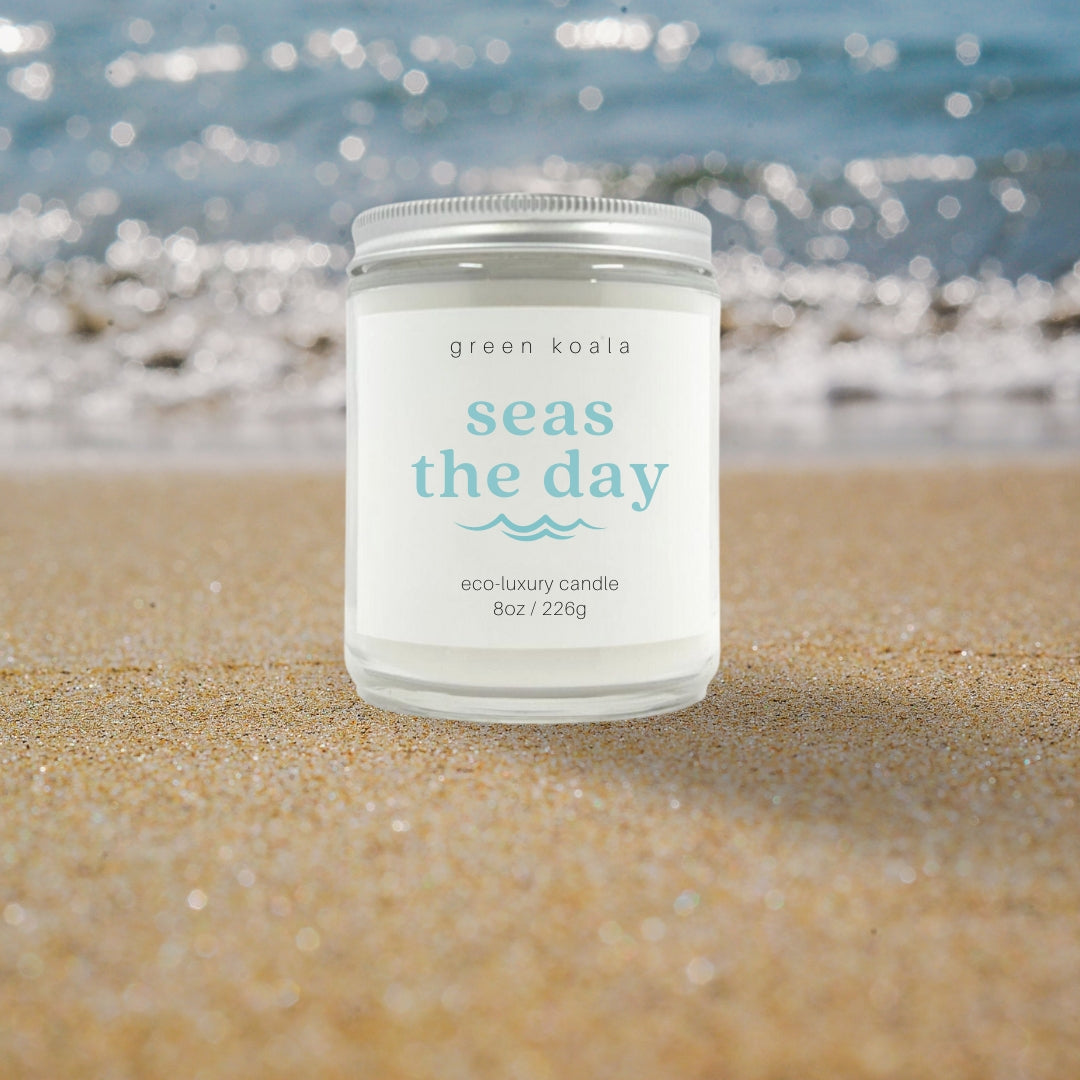 Image of Seas the Day candle in a glass jar with silver lid with a sandy beach background. 