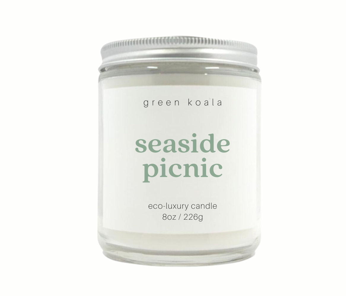 Image of Seaside Picnic candle in a glass jar with silver lid with a white background. 